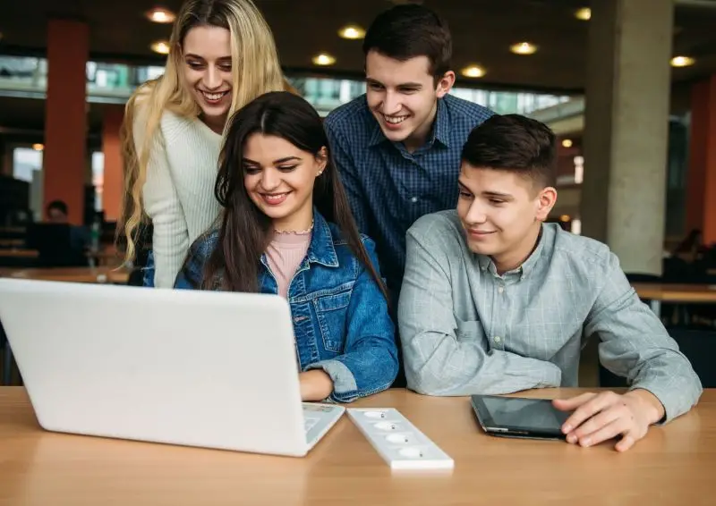 Cuatro estudiantes sonrientes mirando un portátil juntos